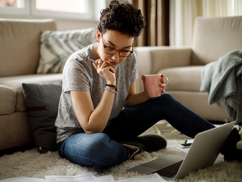 Young woman works at a laptop while sitting on a nicely carpeted floor