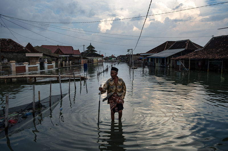 A man wades through calf-deep water on a residential street in Java, Indonesia.