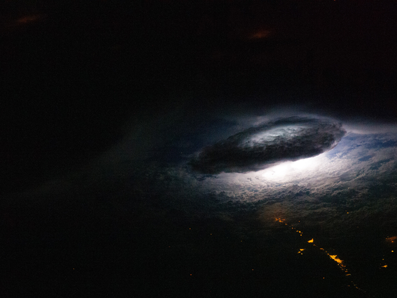 Satellite image of lightning flashing inside a giant thunderstorm over the bright terrestrial lights of Bolivia