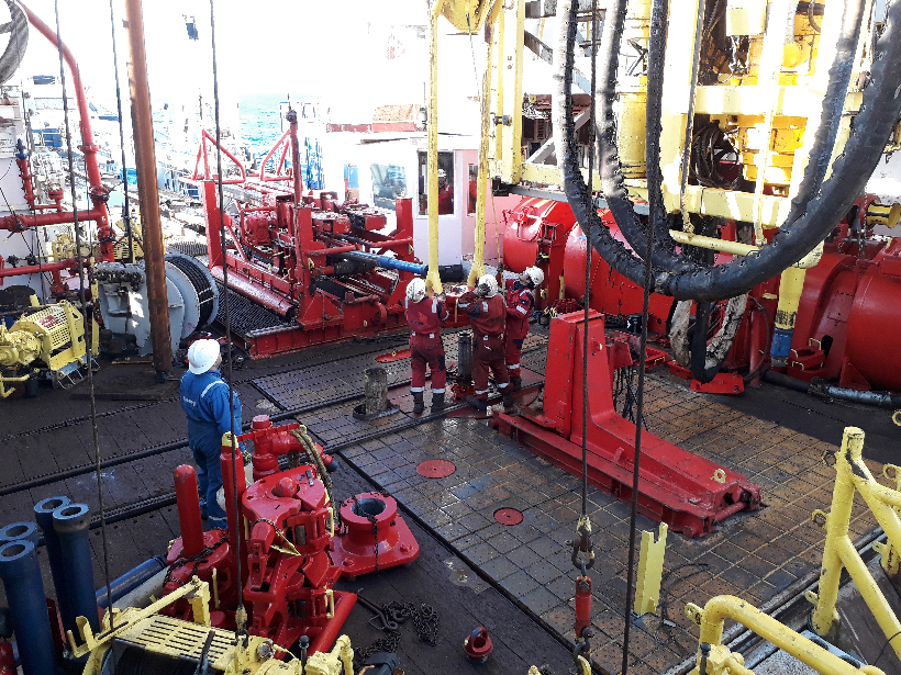 Drillers in hardhats work on the rig floor of a research vessel.