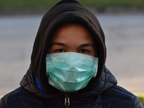 Young man in a hoodie wearing a surgical mask outdoors