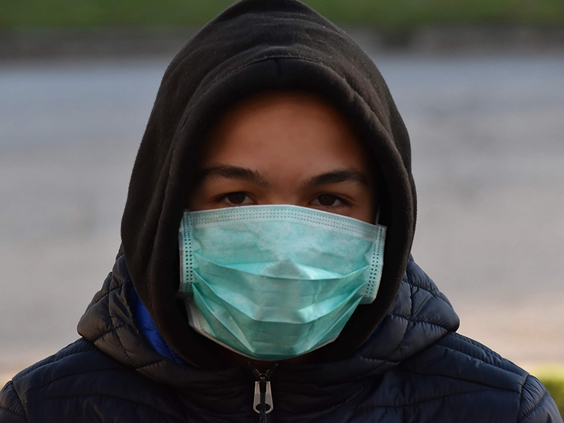 Young man in a hoodie wearing a surgical mask outdoors