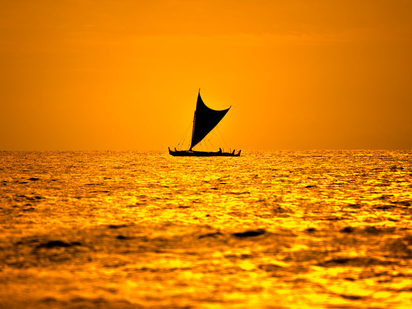 Large outrigger canoe silhouetted against an orange Hawaiian sky