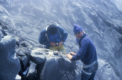 Scientists assess rocks on the top of a smoking volcano. Scientists assess rocks on the top of a smoking volcano.
