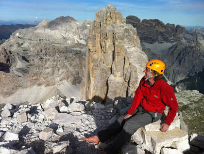 Jörg Robl in a climbing helmet sits at the summit of a high peak