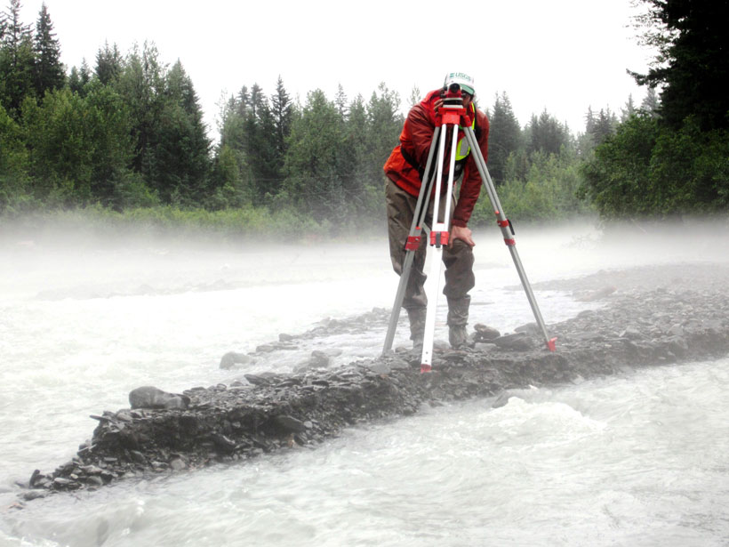 An engineer on a tiny islet uses a total station to survey a rushing stream.