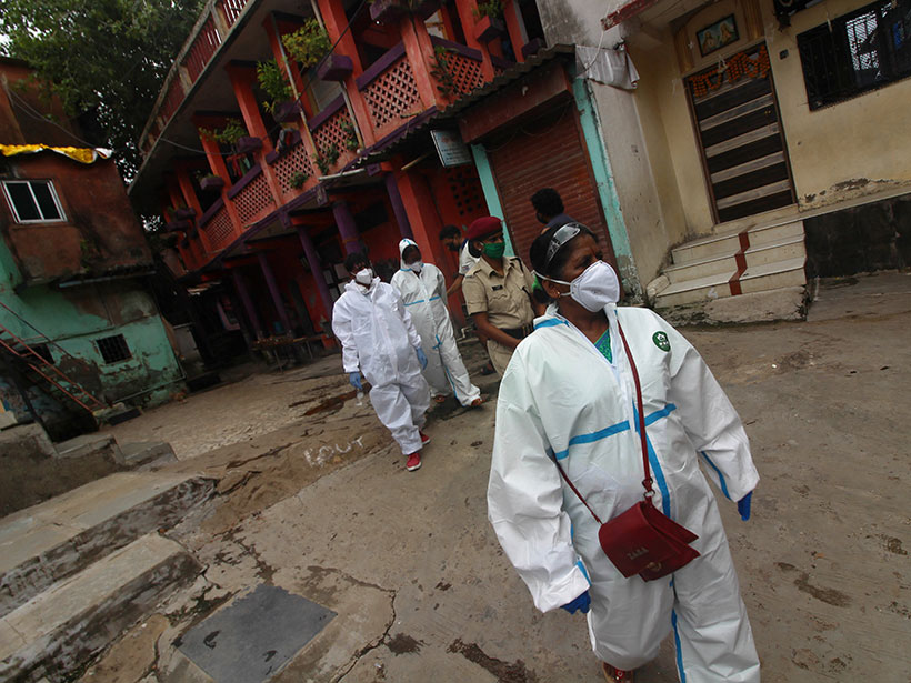 Health care workers in masks and hazmat suits walk through a residential area in India.