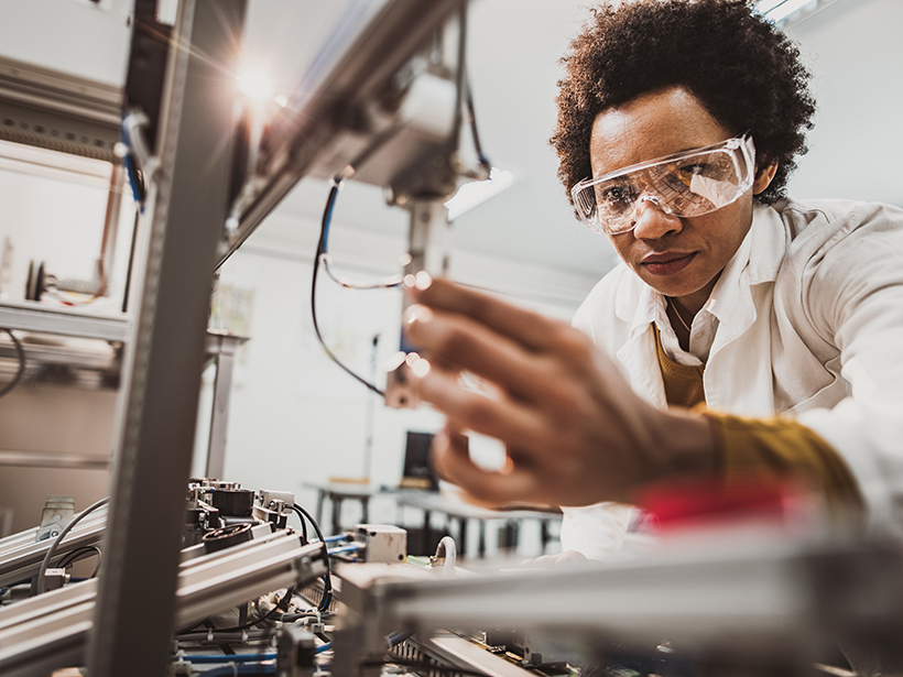 African American woman adjusts a tool in a science lab.