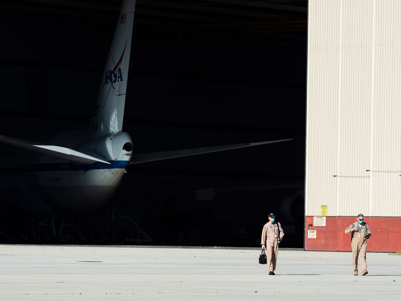Two men walk out of a hangar housing a NASA plane.