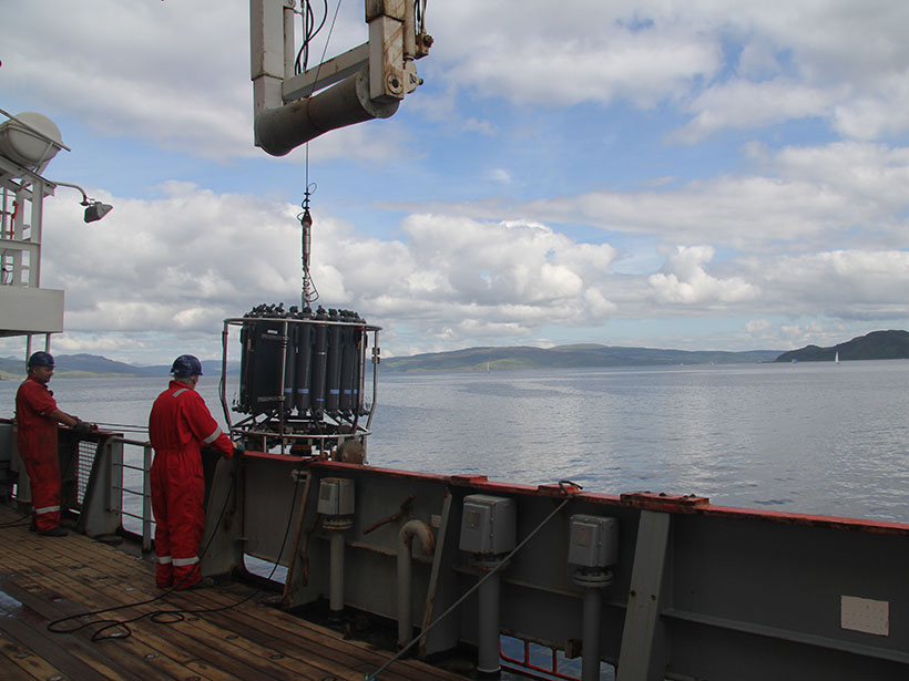 Two researchers look on as a water-sampling device hangs over the side of a research vessel during a cruise to study nitrous oxide emissions.