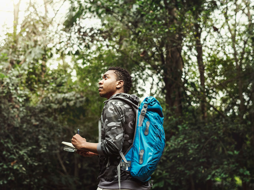 A young Black biologist takes notes outdoors