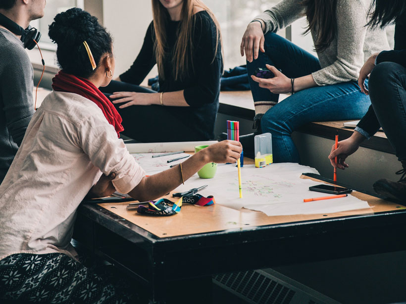 Students sit and stand around a desk with papers and highlighters