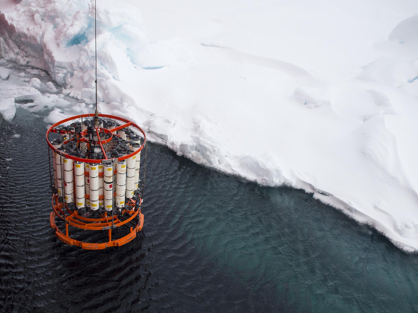 A rosette water sampler hangs from a cable above the Arctic Ocean surface near some sea ice