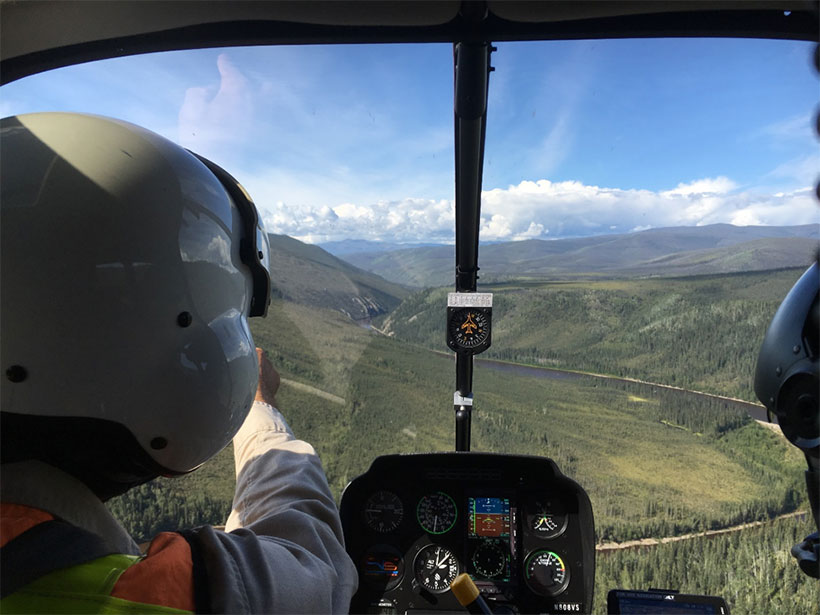 View looking out a helicopter cockpit over remote eastern Alaska landscape