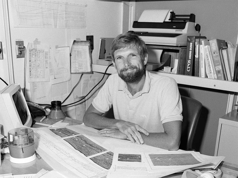 A smiling Casey Moore sits at a desk aboard the drilling vessel JOIDES Resolution