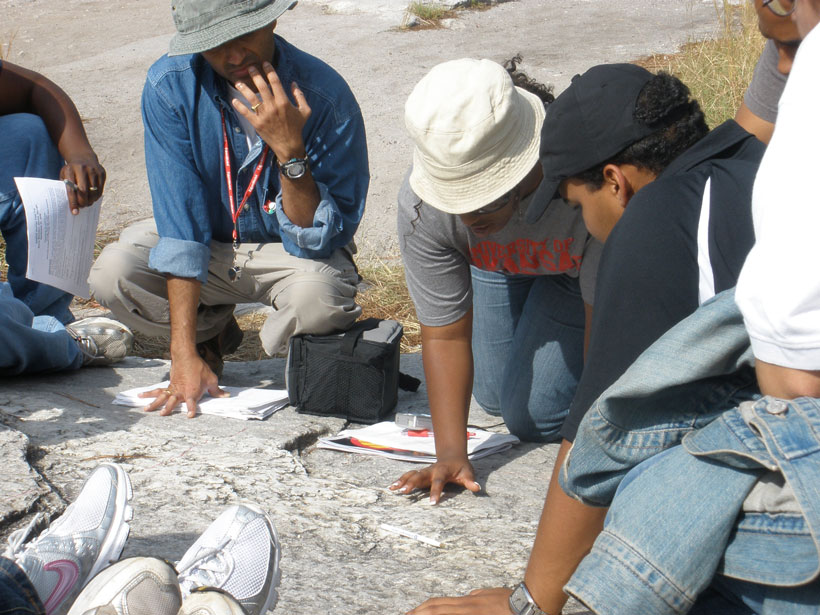 A group of students crouch over a flat rock formation outdoors