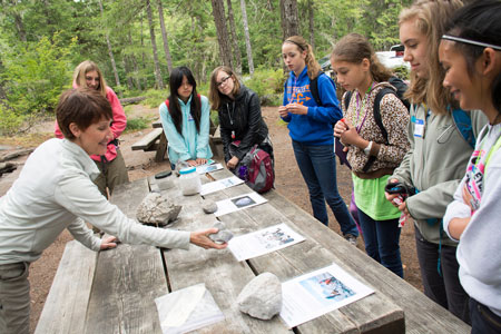 Students look at rock samples and information sheets on a picnic table Students look at rock samples and information sheets on a picnic table