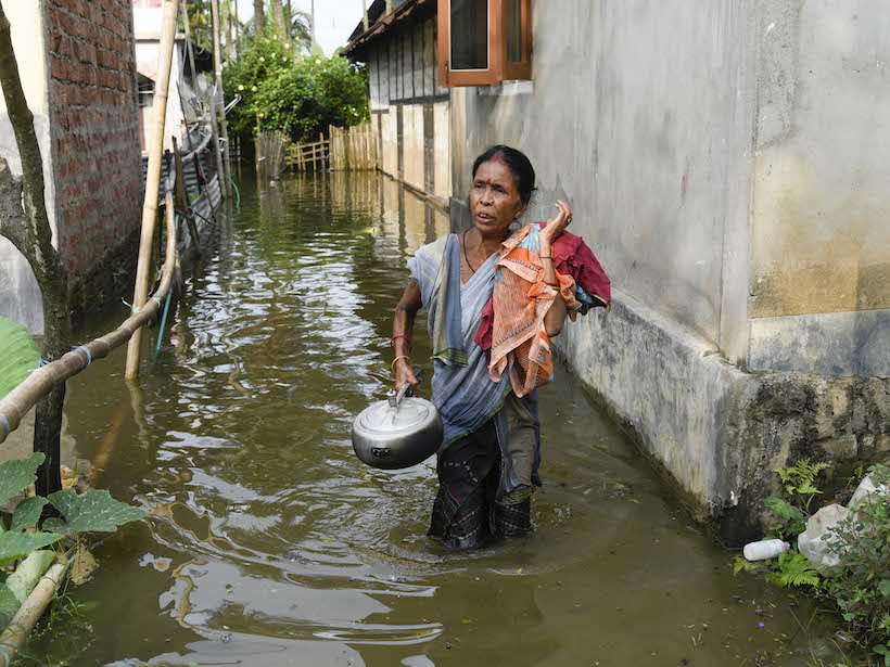 A woman walks through knee-high floodwaters in a narrow street in Assam, India.