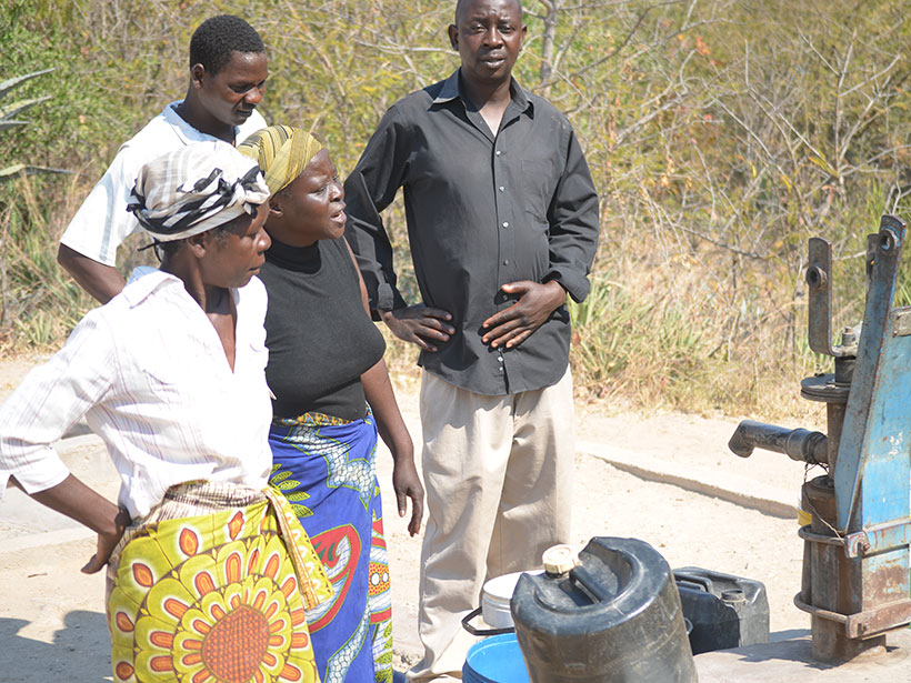 Two men and two women stand near a hand-pumped borehole in Manicaland, Zimbabwe.