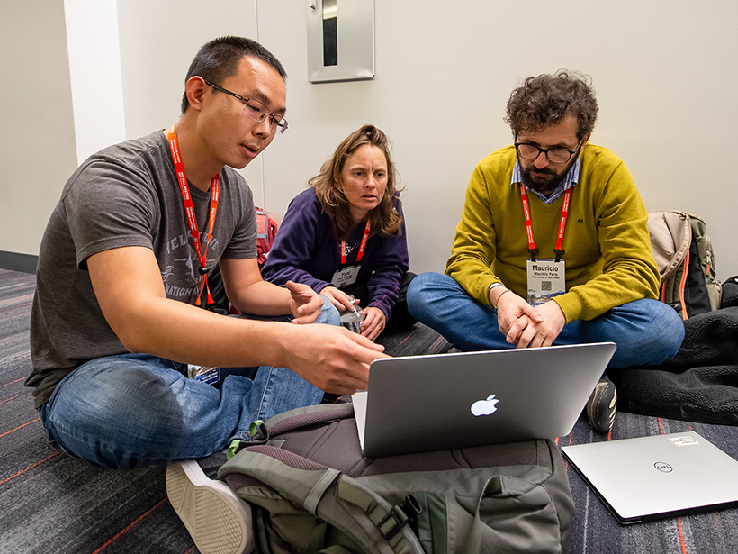 Three scientists sitting on the floor around a laptop