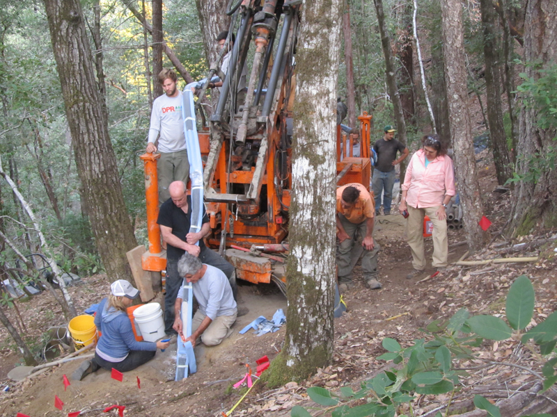 Researchers use heavy machinery to install a monitoring tube into the ground in a forest.