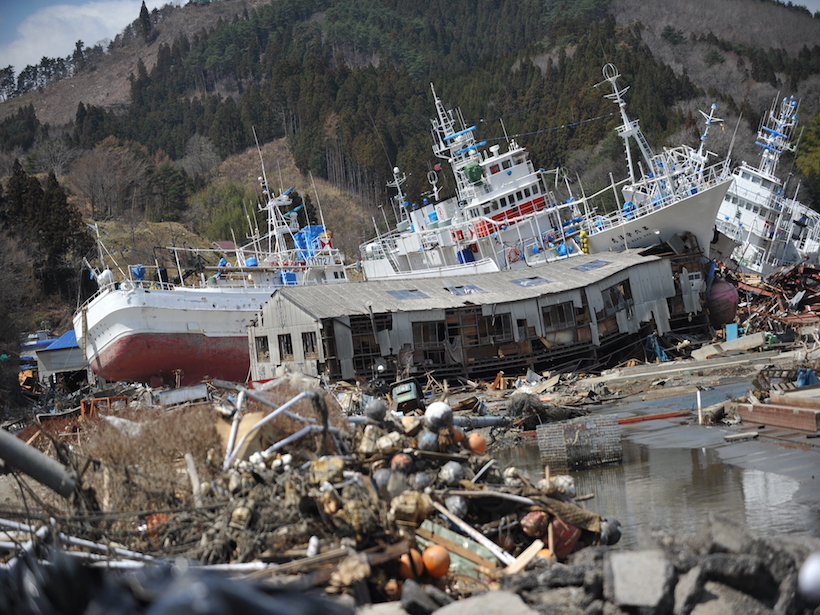 Deformed buildings, beached boats, and debris litter a coastline in Japan.