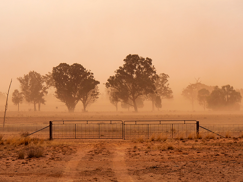 A metal gate across a rural road during a dust storm in a dry landscape