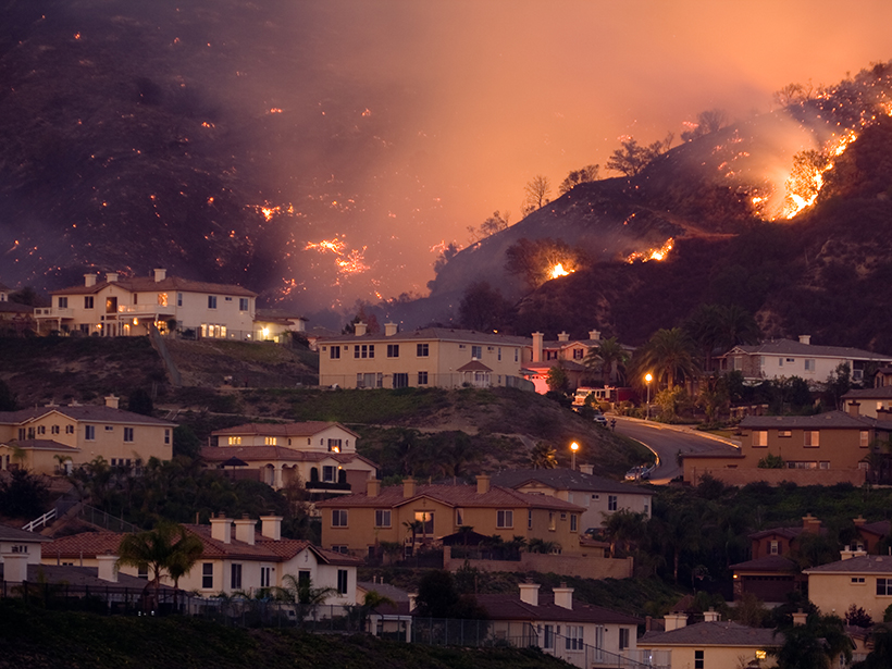 Homes on a hillside with fires in the background