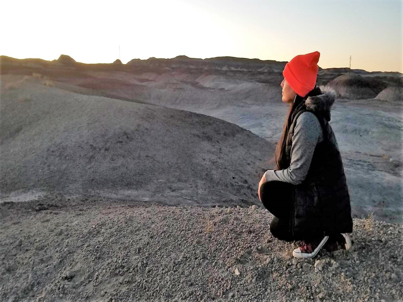 A woman in profile kneels, looking out over Indigenous land in Arizona.
