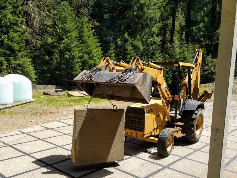 A backhoe loader lifts a concrete block using chains. A backhoe loader lifts a concrete block using chains.