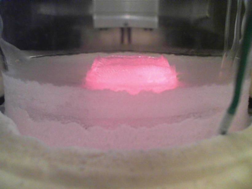 A pink laser sublimates an ice core in a scientific instrument chamber.