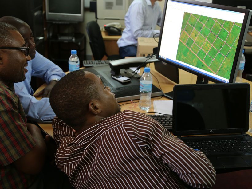 Three men gather around a desktop computer monitor.