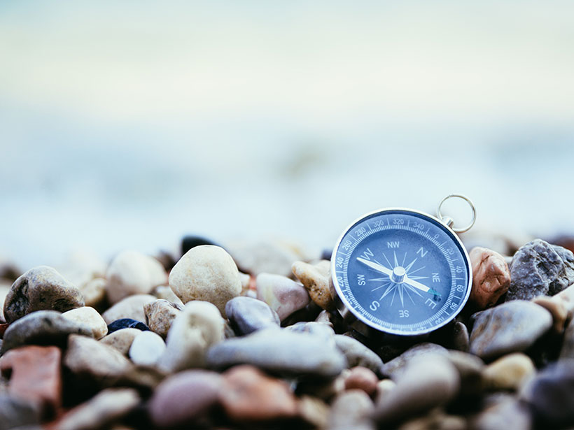A handheld compass sits amid rocks on a beach