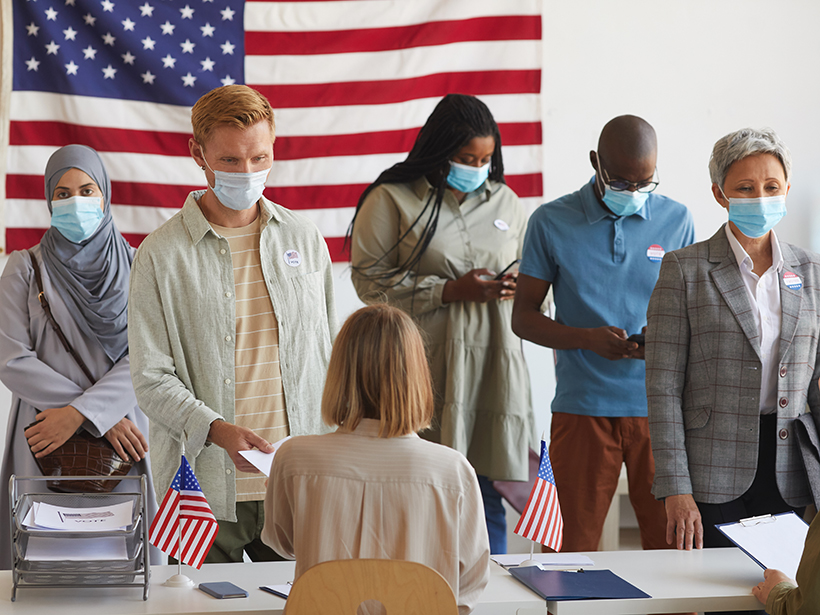 Multiethnic group of people standing in a row and wearing masks at a polling station on Election Day