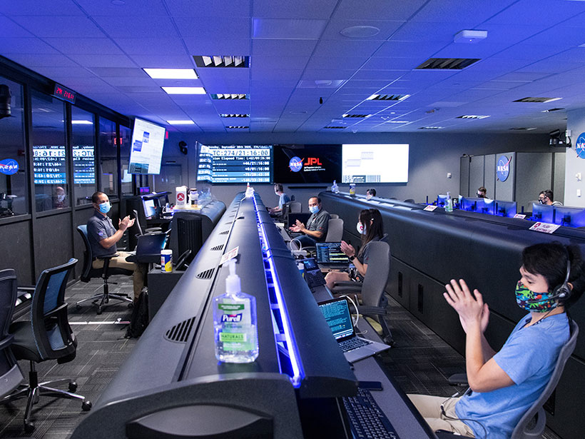 A NASA mission control room sparsely staffed with masked scientists