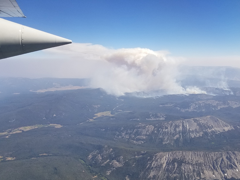 Aerial view of a wildfire smoke plume rising from a mountainous landscape
