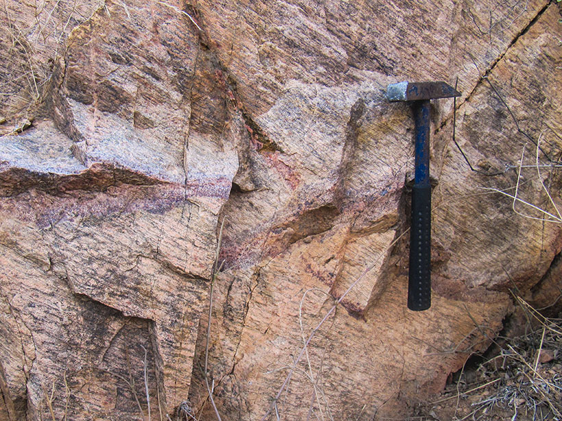 Close up of an outcrop of pink cratonic rock with a rock hammer for scale
