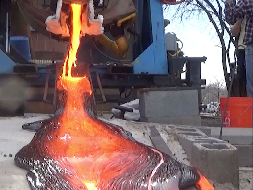 A large magma furnace pours a mixture of silicate and metallic lava onto a flat surface, with a pool of semicooled lava flowing. The lava is black, orange, yellow, and silver.