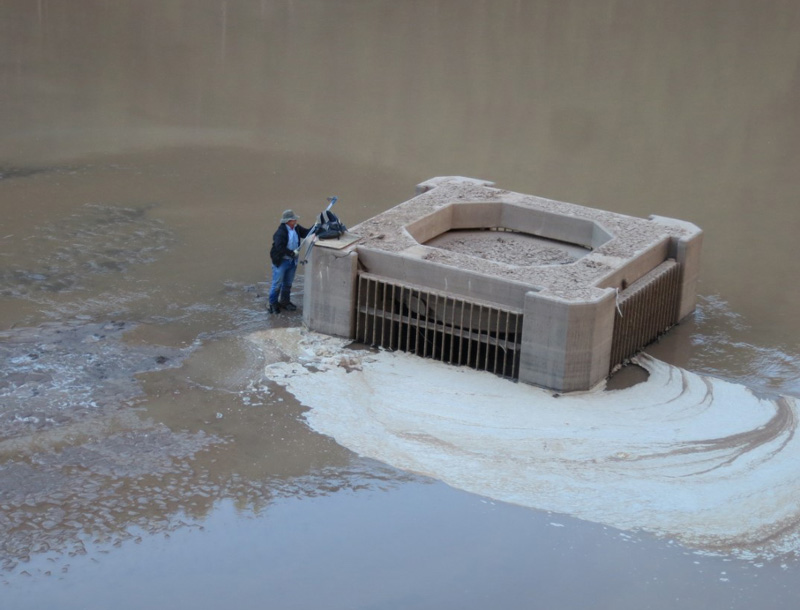 A person stands beside the top of a sediment outlet structure that is almost entirely buried.