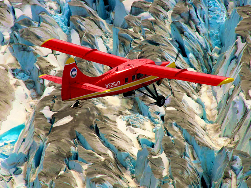 A photograph of a plane flying over mountain glaciers in Alaska