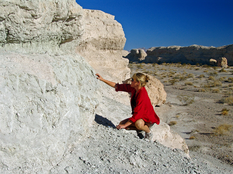A geologist crouches next to an outcrop of white rocks with a desert landscape in the background. A geologist crouches next to an outcrop of white rocks with a desert landscape in the background.