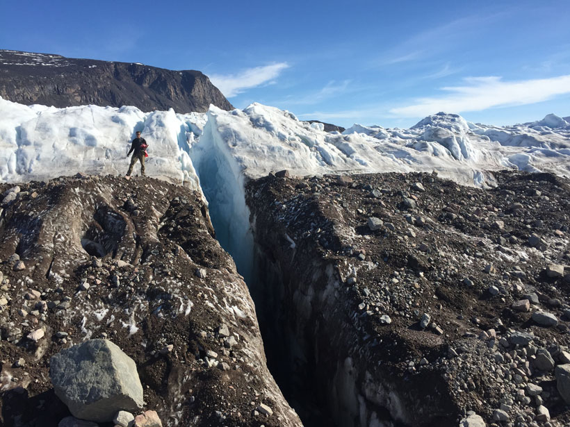 A researcher standing beside a rift in a glacier A researcher standing beside a rift in a glacier