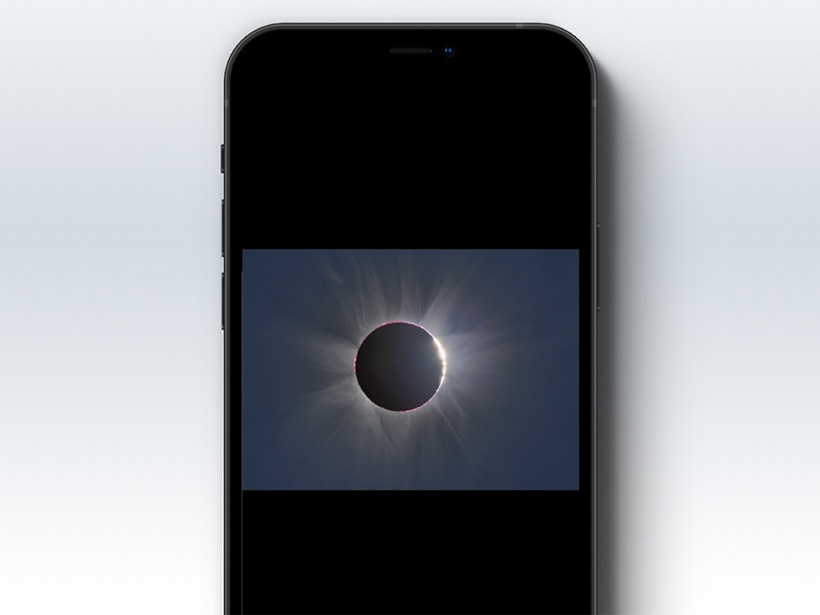 A smartphone on a white background shows an image of the Sun just after totality during the August 2017 total solar eclipse. The Sun’s corona appears as bright white wisps and beams around the black circle of the Moon. Along the right edge of the black circle, a string made of bright points of sunlight shines through the ragged edge of the Moon’s disk in a phenomenon known as Baily’s beads.