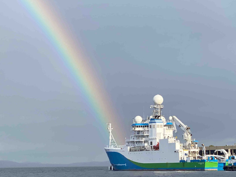 A large ship sits in the water docked at port with a rainbow in the background