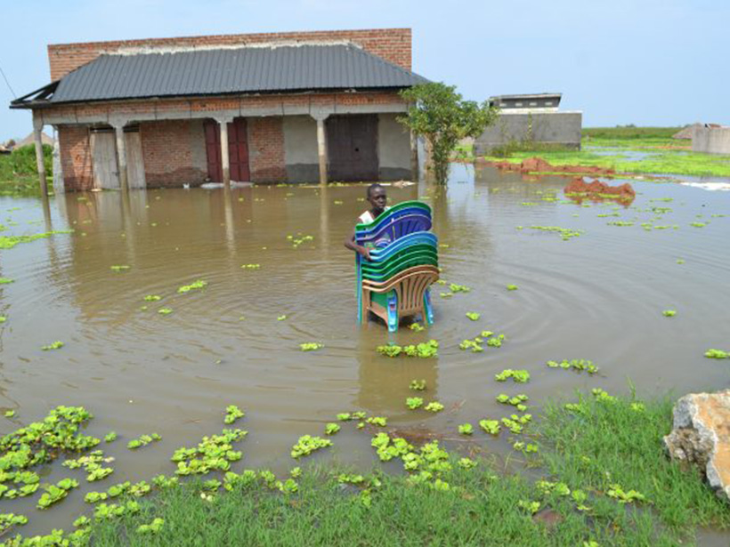 Image of a person carrying plastic chairs through floodwaters in Buliisa, Uganda
