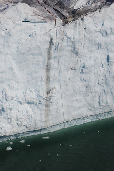 A narrow cord extends over the edge of a tall glacial ice cliff into the water below A narrow cord extends over the edge of a tall glacial ice cliff into the water below