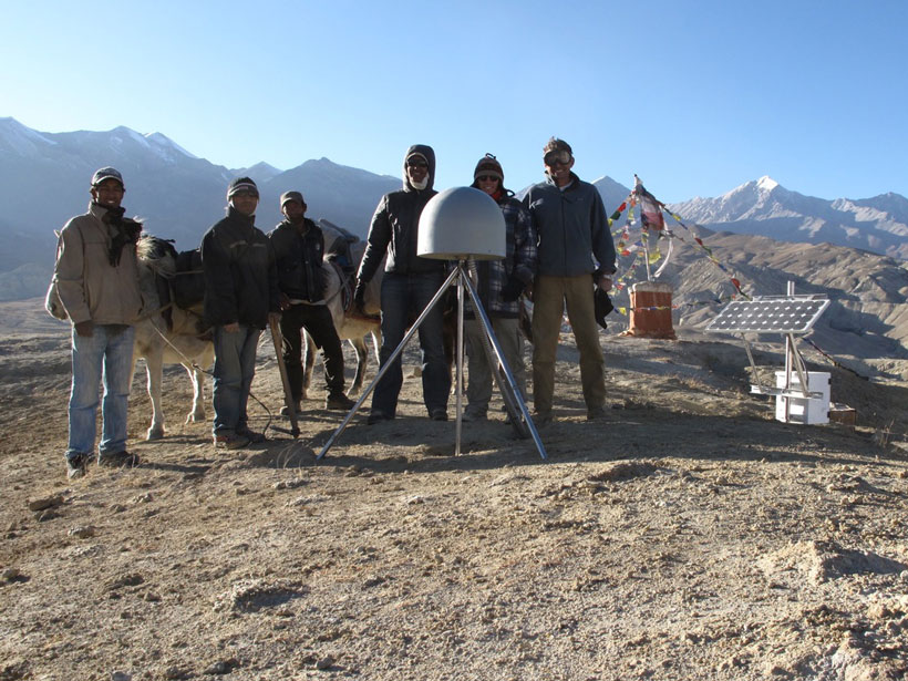 Research scientists pose in the Himalayas with a GNSS station.