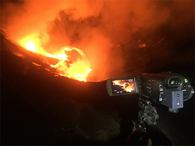 A video camera (foreground) stands above a glowing orange lava lake