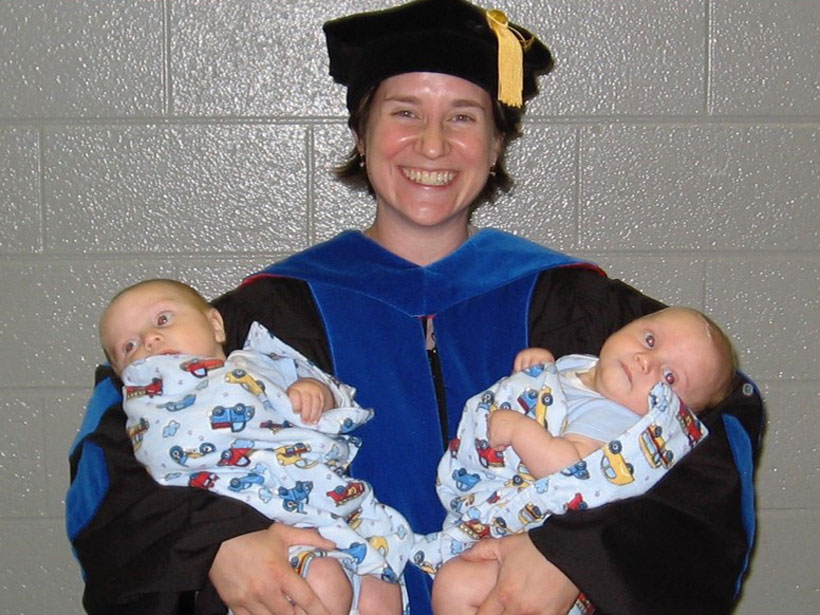 Karen Layou wearing academic regalia and holding her 3-month-old twins