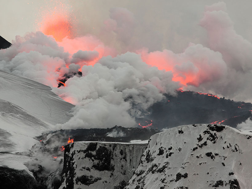 Snow-covered Fimmvörðuháls, close to Eyjafjallajökull, where white ash and steam are tinged red by lava erupting from a fissure